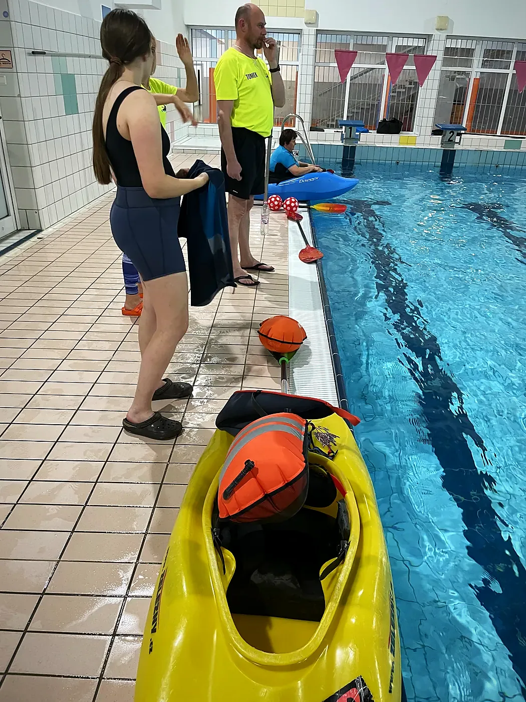 Instruktorzy przy basenie, kajakarz w żółtym kajaku